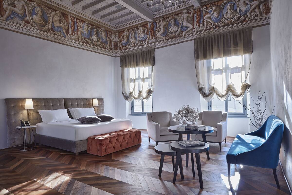 A hotel room with a large bed, two armchairs, a small table, and a blue sofa.