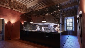A modern kitchen with a large glass partition, overhead lighting, and a rustic ceiling. - Vistaterra (Parella)