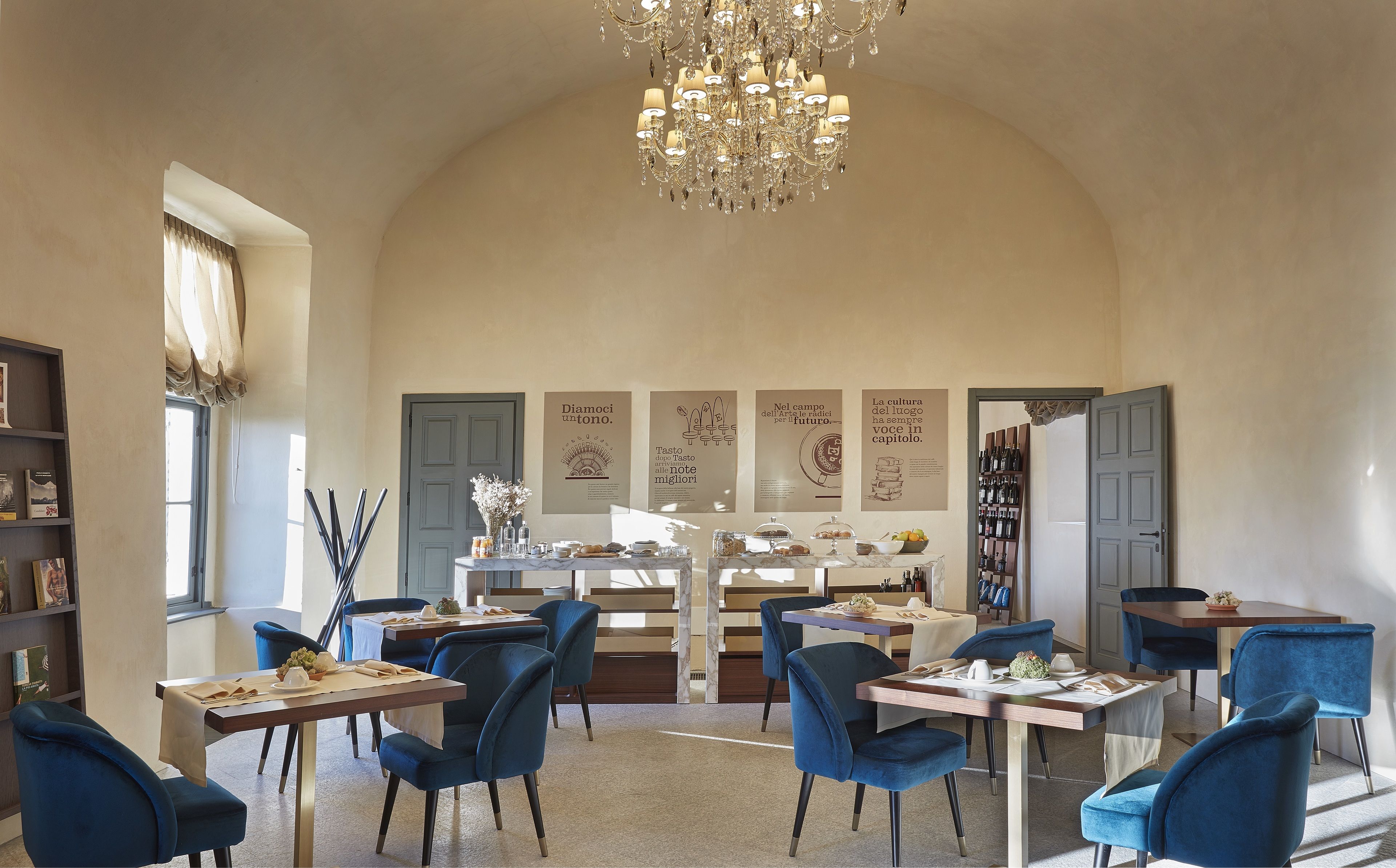 Un coin repas avec des chaises bleues, un lustre et une table dressée avec des assiettes et des verres.