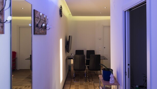 A hallway with a patterned carpet, a mirror, a clock, and a television on the wall. - Senator Flats (Vienna)