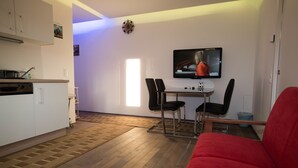 A compact living space with a kitchenette, a dining area with two chairs, a red sofa, and a TV mounted on the wall. - Senator Flats (Vienna)