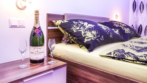 A bedroom with a wooden bed, floral pillows, a bottle of Moët & Chandon champagne, and two wine glasses on a bedside table. - Senator Flats (Vienna)