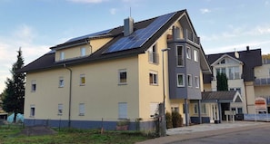 Edificio residencial con paneles solares, balcón y un pequeño jardín.