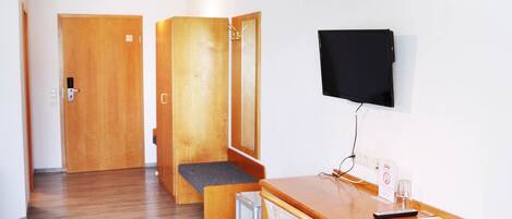 A hotel room with a wooden desk, a television mounted on the wall, and a door leading to another room.