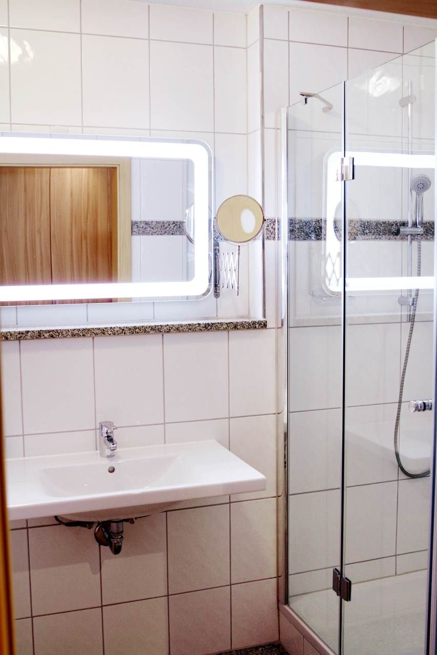 Un baño con un lavabo blanco, un espejo y una ducha con mampara de vidrio.