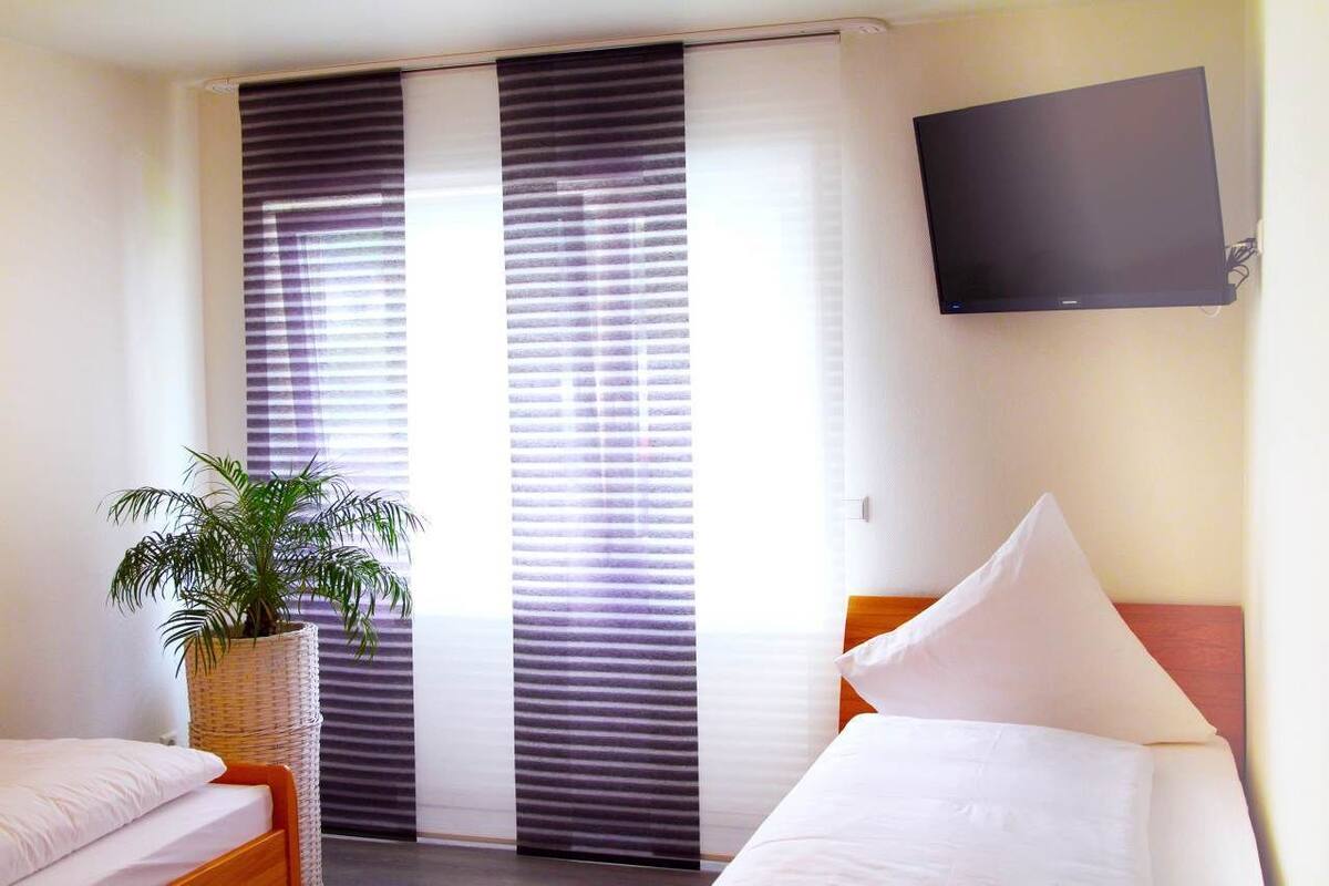 Una habitación de hotel con una cama, un televisor montado en la pared y una ventana con persianas.
