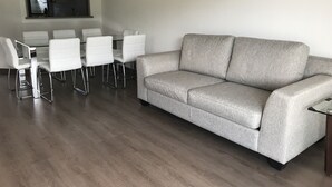 A modern living room with a grey sofa, white chairs, and a glass dining table. - Condominio Costa Pucon (Pucón)