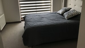 A bedroom with a bed, two pillows, a radiator, and a window with blinds. - Condominio Costa Pucon (Pucón)