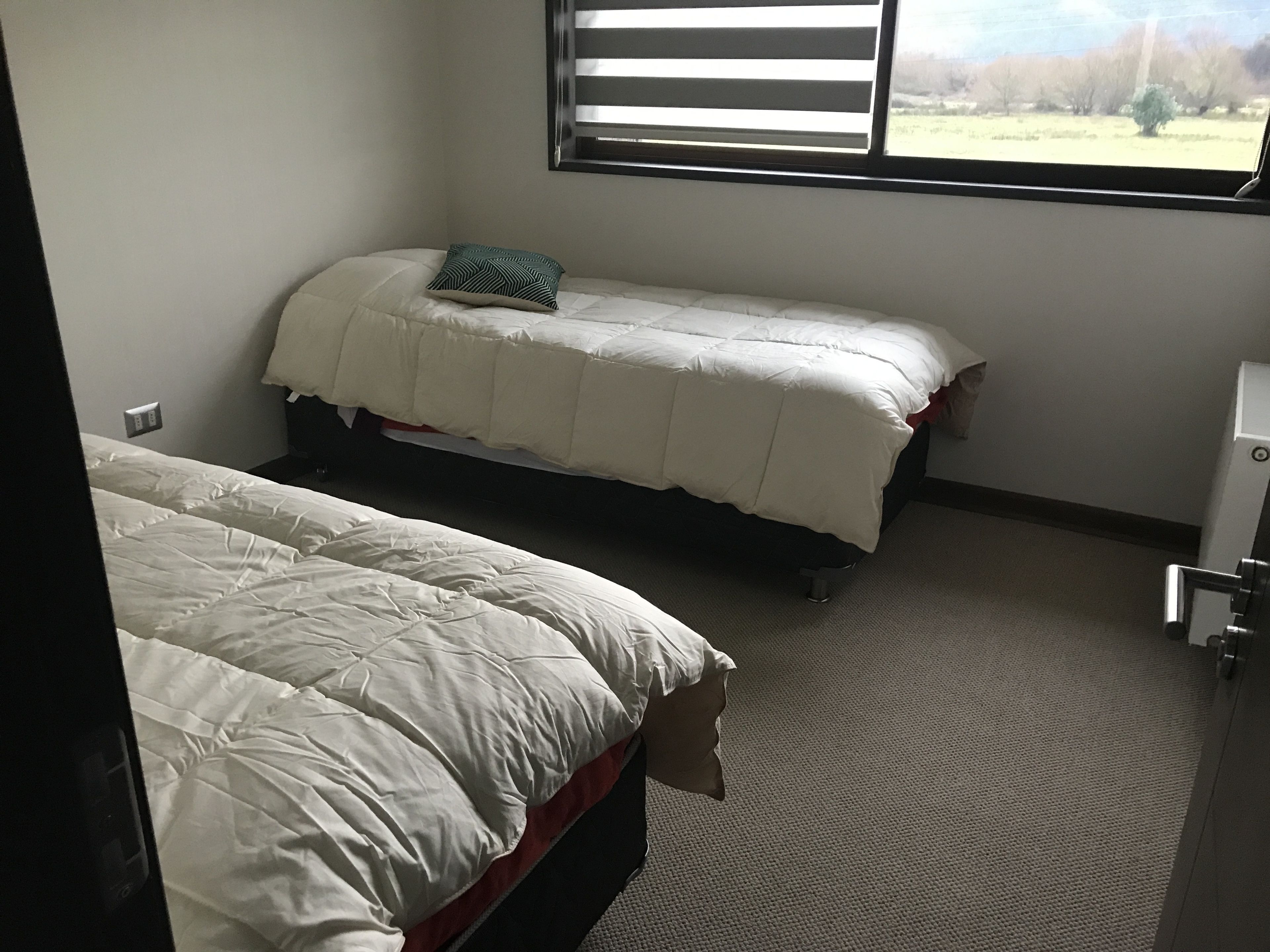 Un dormitorio con dos camas, una ventana con persianas y suelo alfombrado.