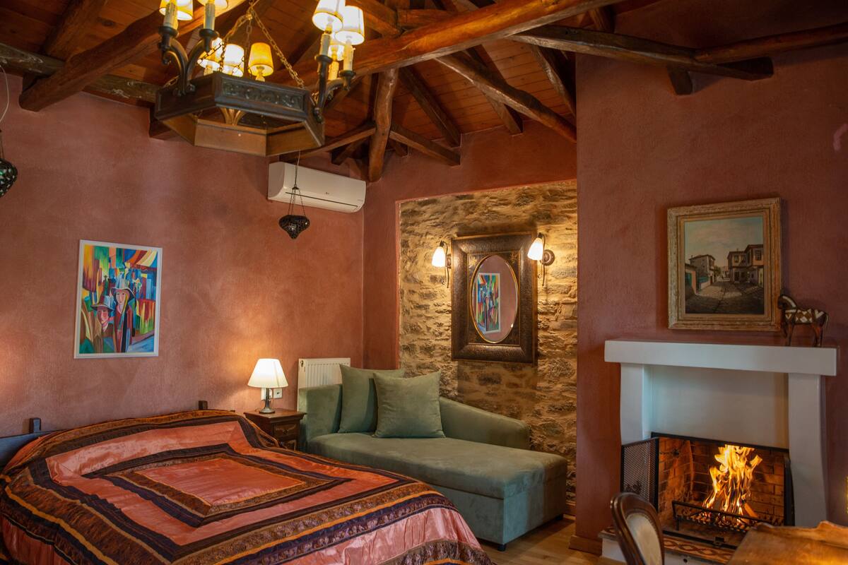 Una habitación acogedora con cama, sofá verde, chimenea y obras de arte en las paredes.