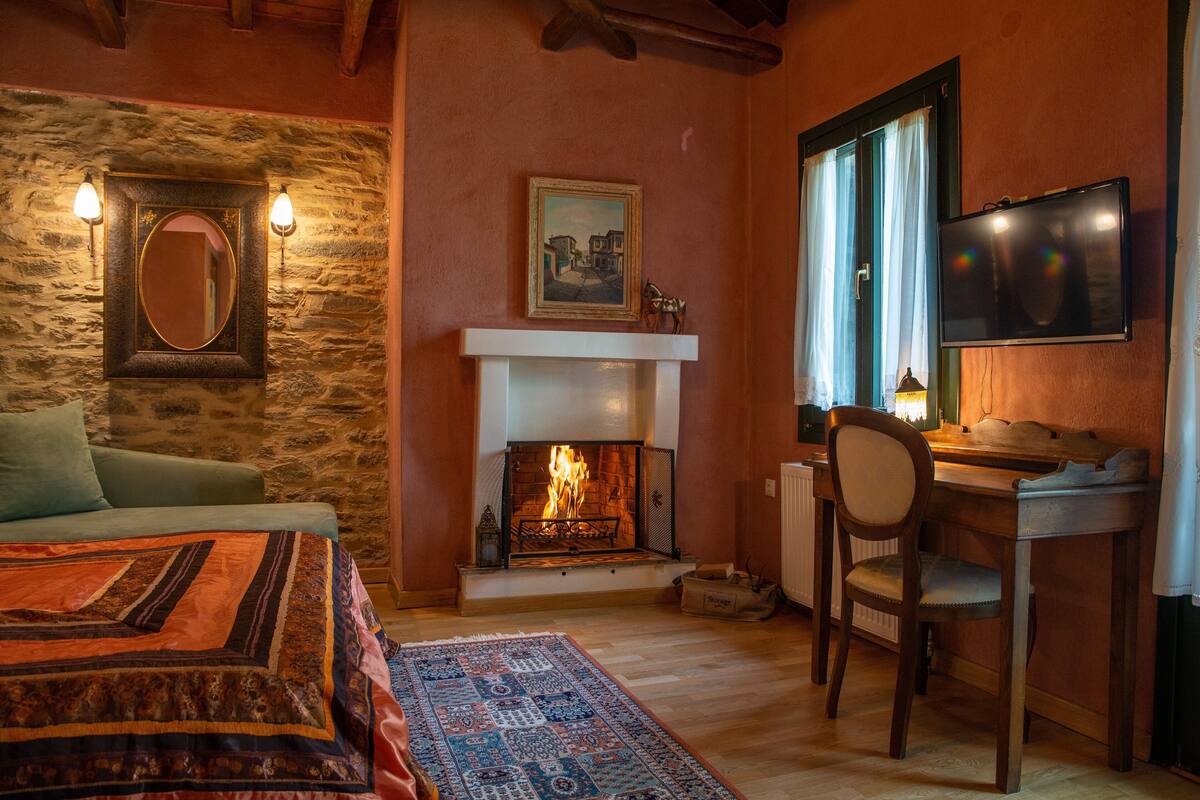 Una habitación acogedora con chimenea, cama, escritorio y televisor.
