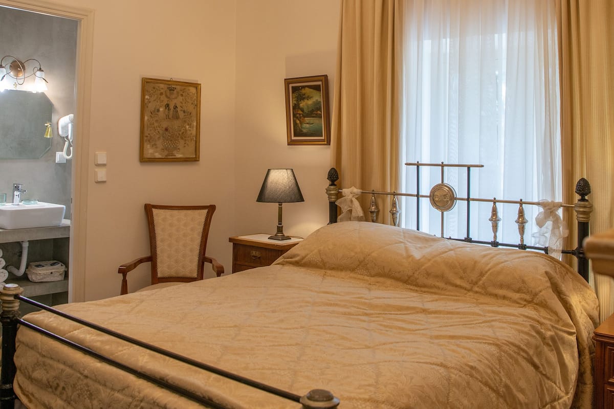 Un dormitorio con una cama grande, una araña, una silla, una mesita de noche y una ventana con cortinas.