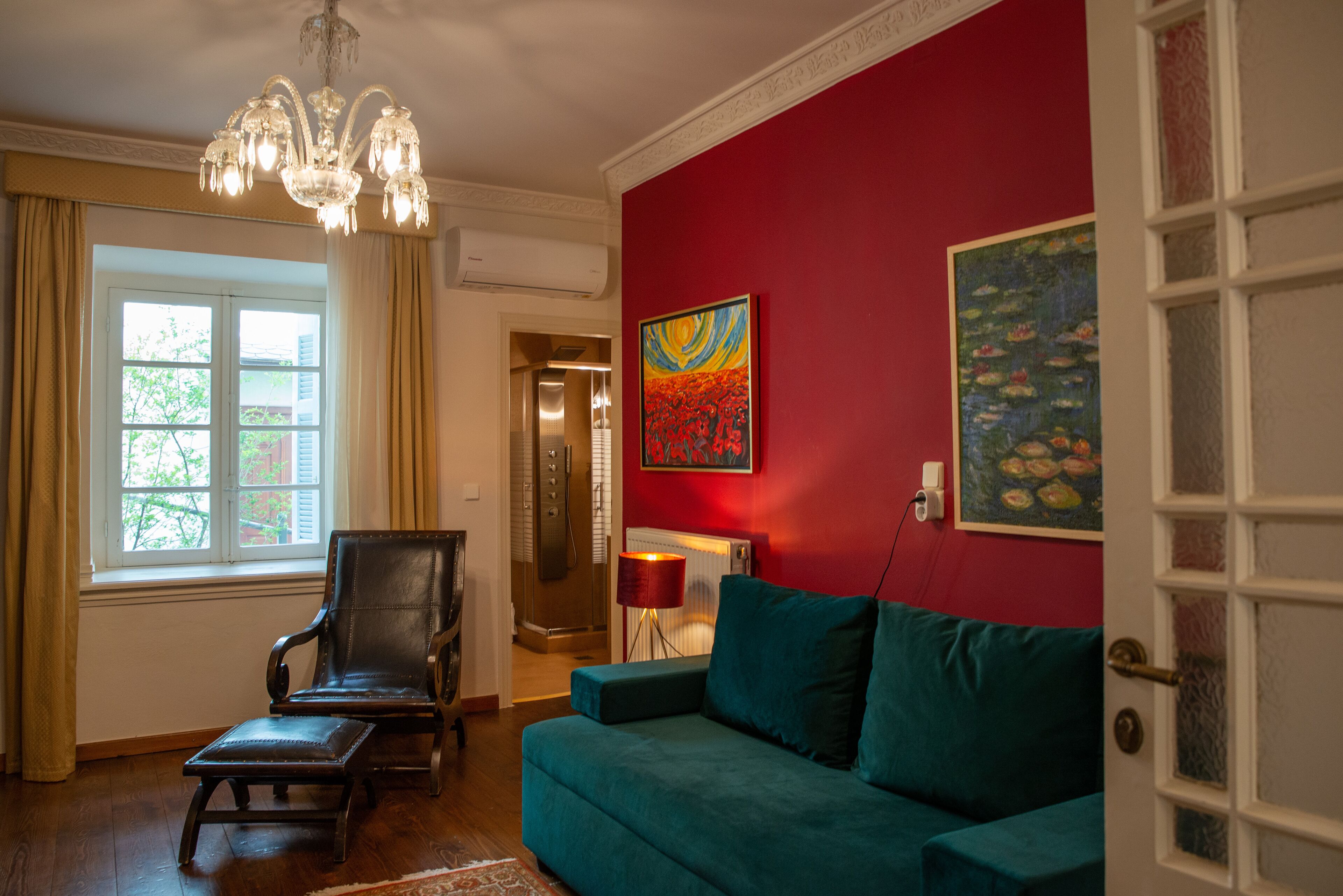 A living room with a teal sofa, a wooden chair, a chandelier, and artwork on the walls.