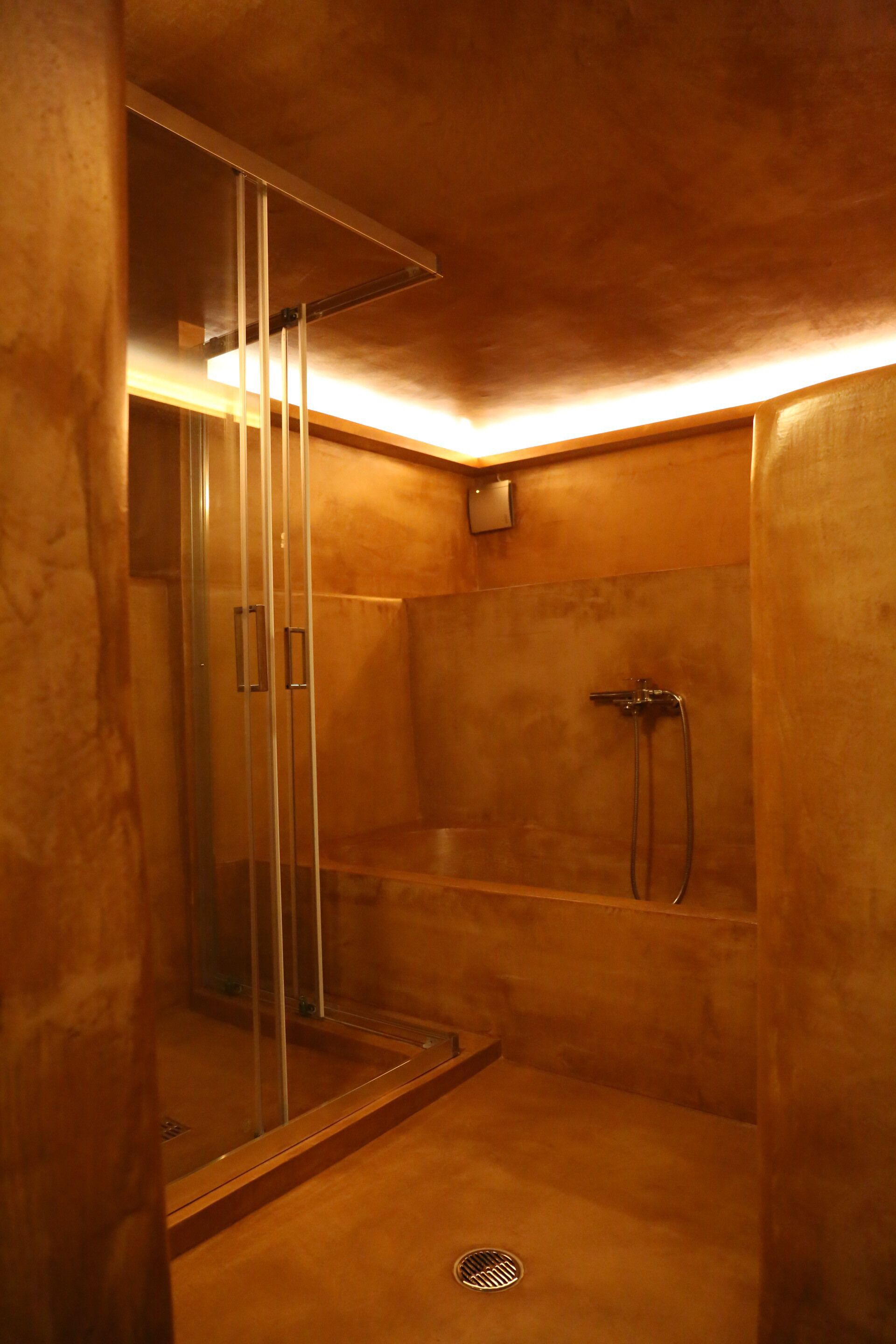 A walk-in shower with a glass door, a handheld showerhead, and a wall-mounted control panel.