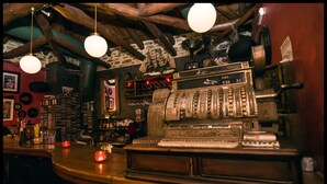 Eine alte Kasse mit dem Aufdruck "Los 455" in einer Bar, mit Holzbalken und hängenden Lampen.