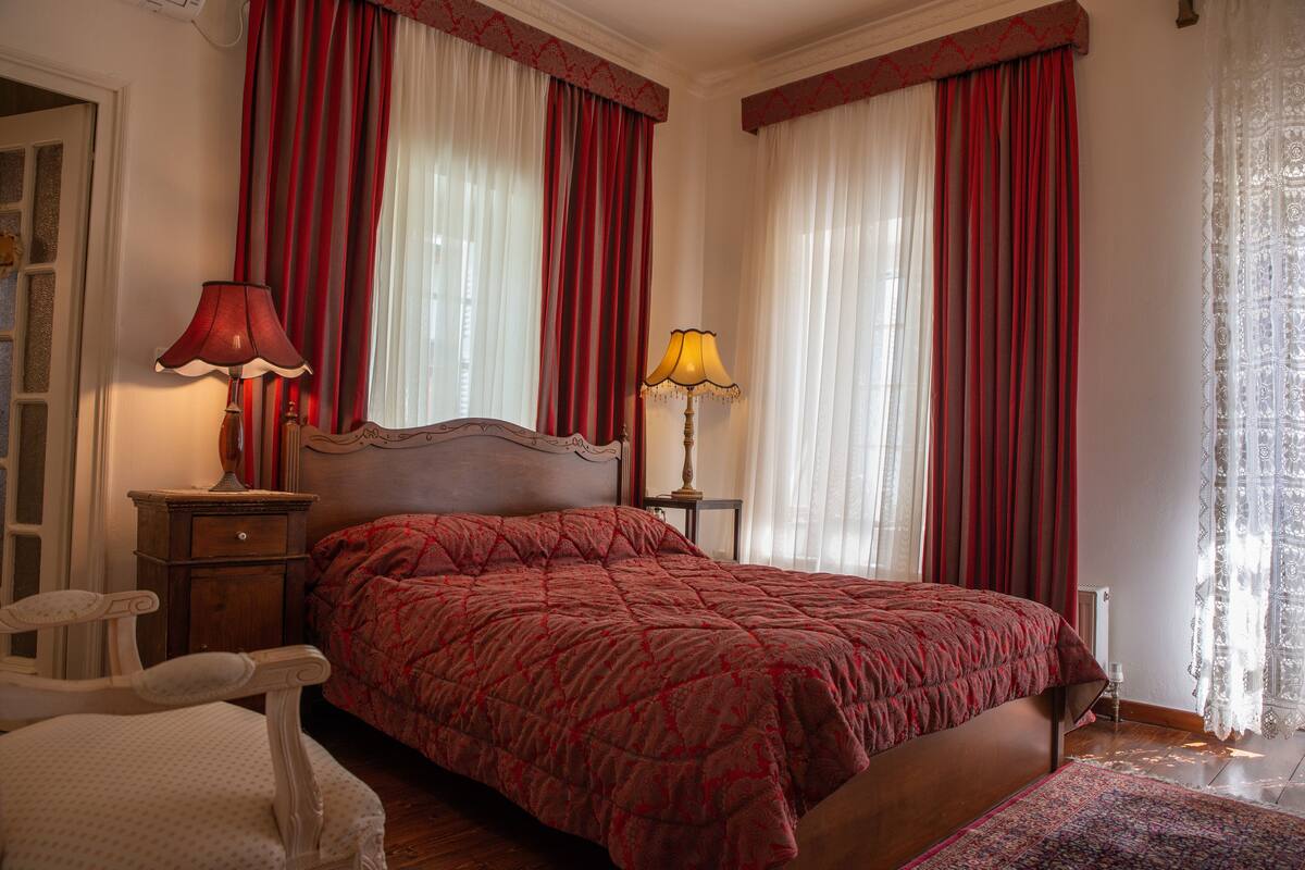 Un dormitorio con una cama, dos mesitas de noche, una silla y una ventana con cortinas.