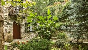 Ein Steinhaus mit Holztür, einem Balkon und einem Garten mit verschiedenen Pflanzen und Blumen.