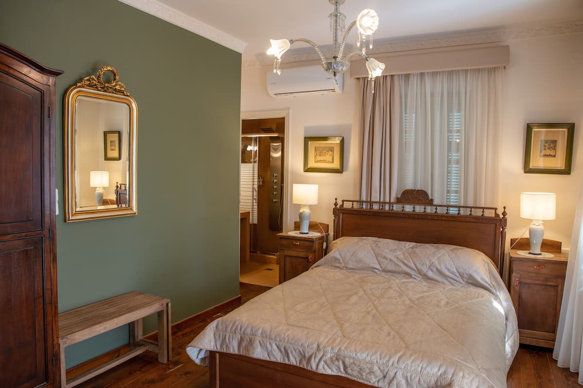 Un dormitorio con una cama grande, un banco de madera, un espejo y dos mesitas de noche con lámparas.