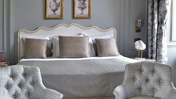 A neatly arranged bedroom with a bed, two armchairs, a coffee table with breakfast items, and framed artwork on the wall.
