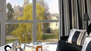 A room with a large window offering a view of a cathedral and trees. A table with breakfast items is visible. - Villa Lara Hôtel (Bayeux)