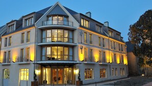 A multi-story hotel with a prominent corner balcony, large windows, and a well-lit entrance. - Villa Lara Hôtel (Bayeux)