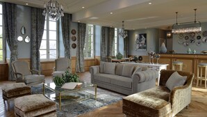 A spacious living room with a large sofa, armchairs, and ottomans, a glass coffee table, and a chandelier. - Villa Lara Hôtel (Bayeux)
