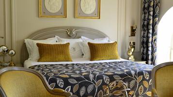 Un dormitorio elegante con una cama grande, dos retratos enmarcados, una araña y muebles clásicos.
