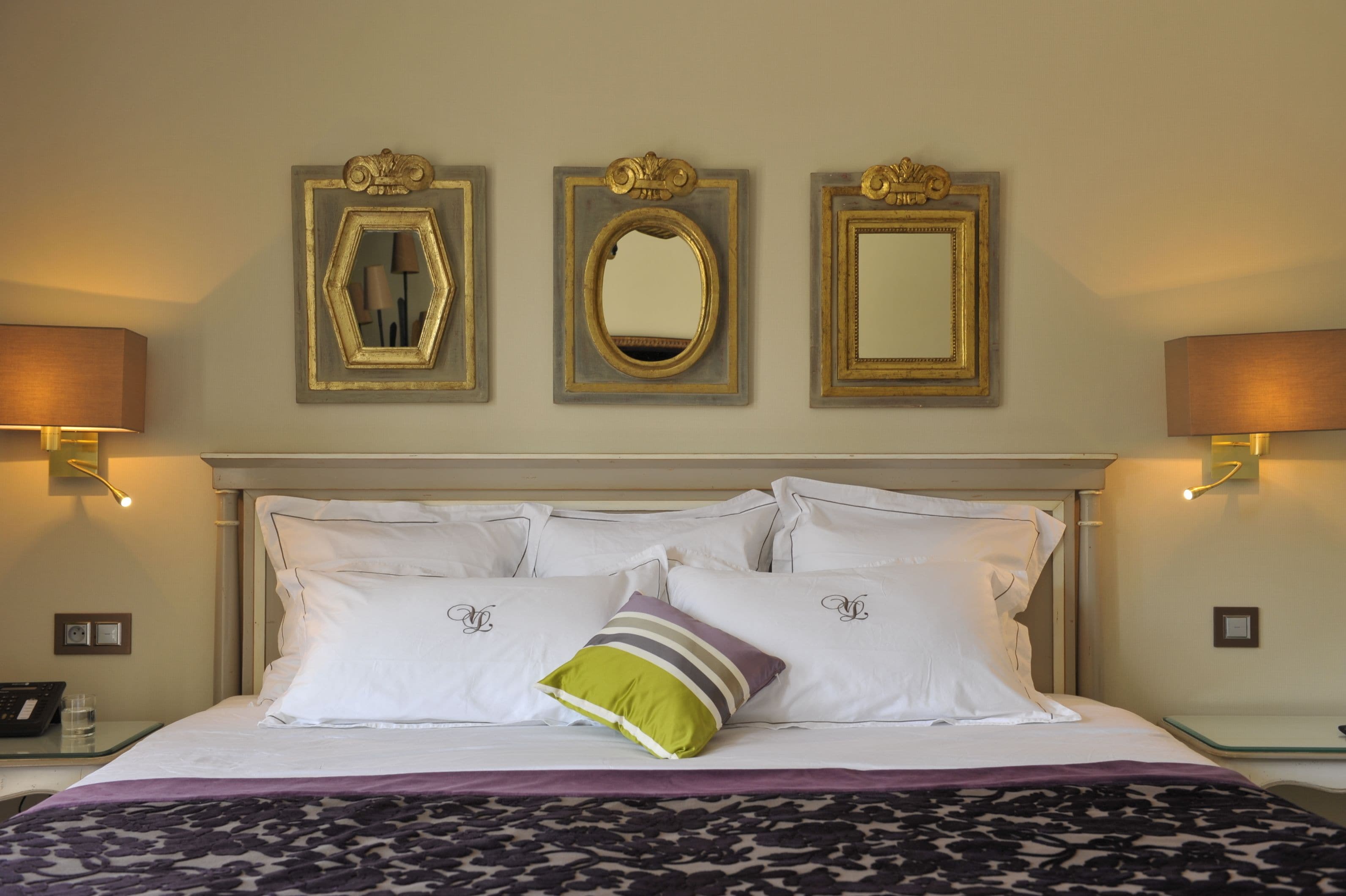A hotel room with a bed, three wall-mounted mirrors, and two bedside lamps.