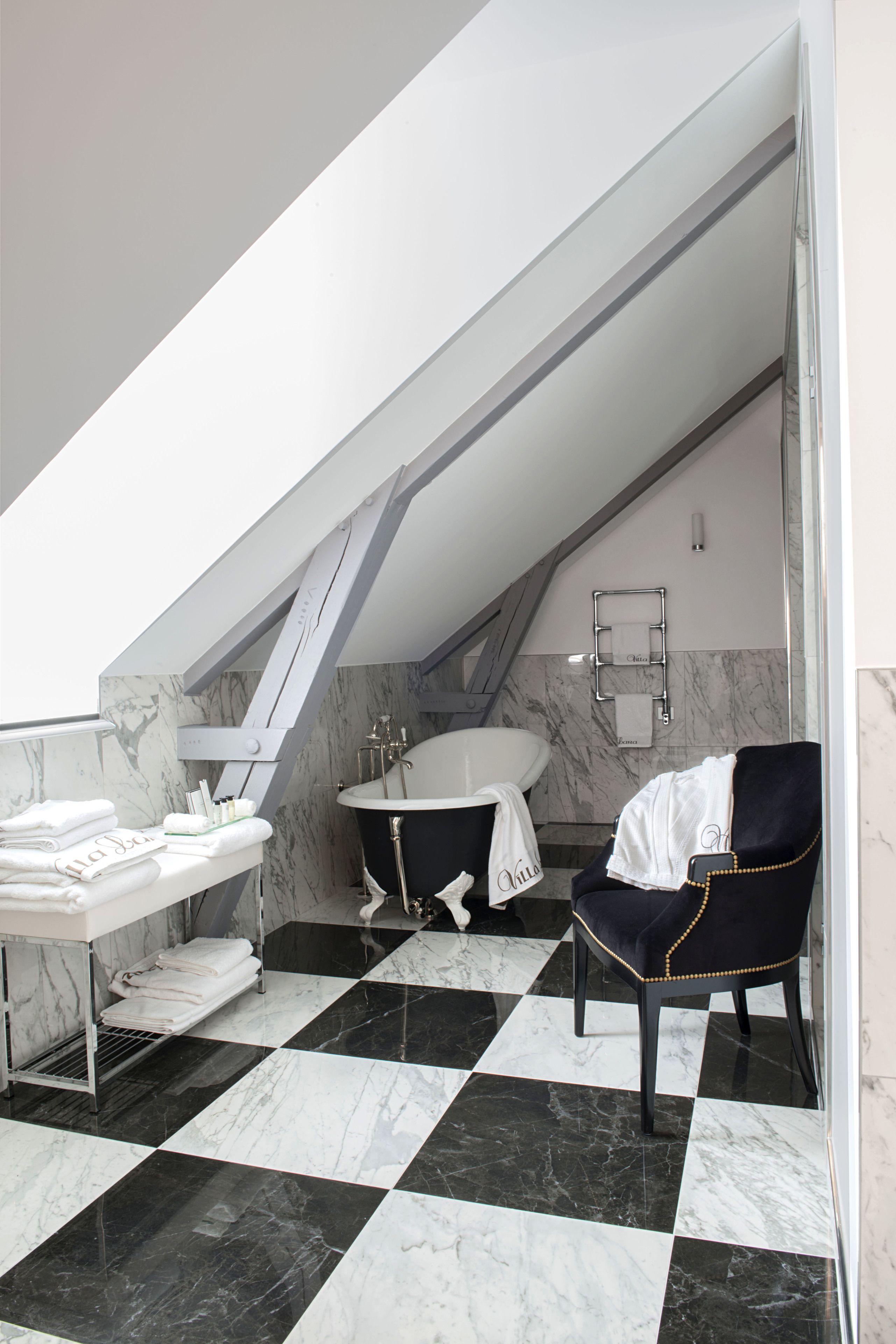Un baño moderno con piso a cuadros, una bañera, un lavamanos y una silla.