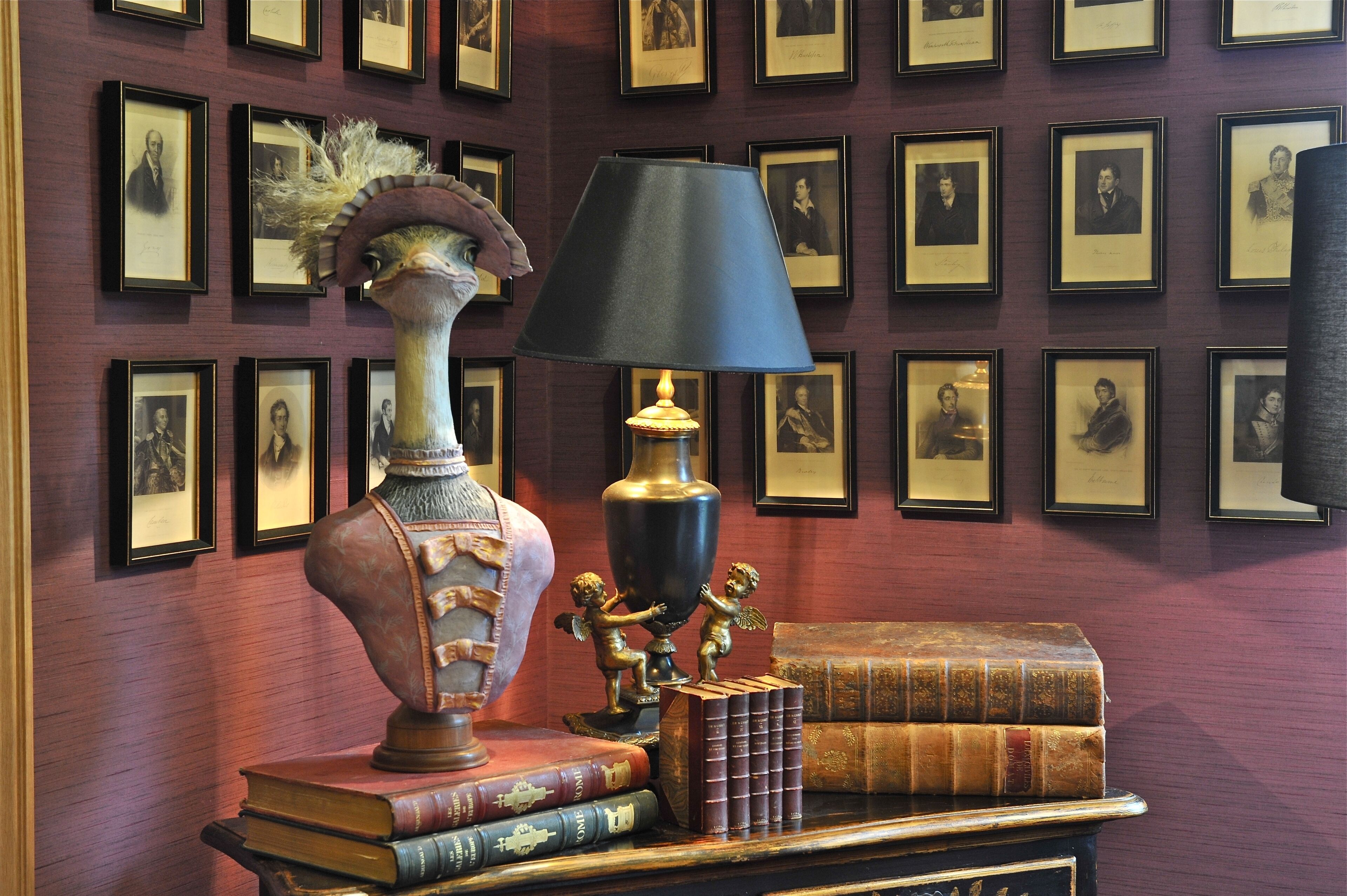 A room with a wall of framed photographs, a bust sculpture, a lamp, and several books.
