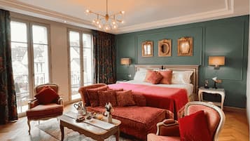 A spacious bedroom with a large bed, two armchairs, a wooden coffee table, and a chandelier.