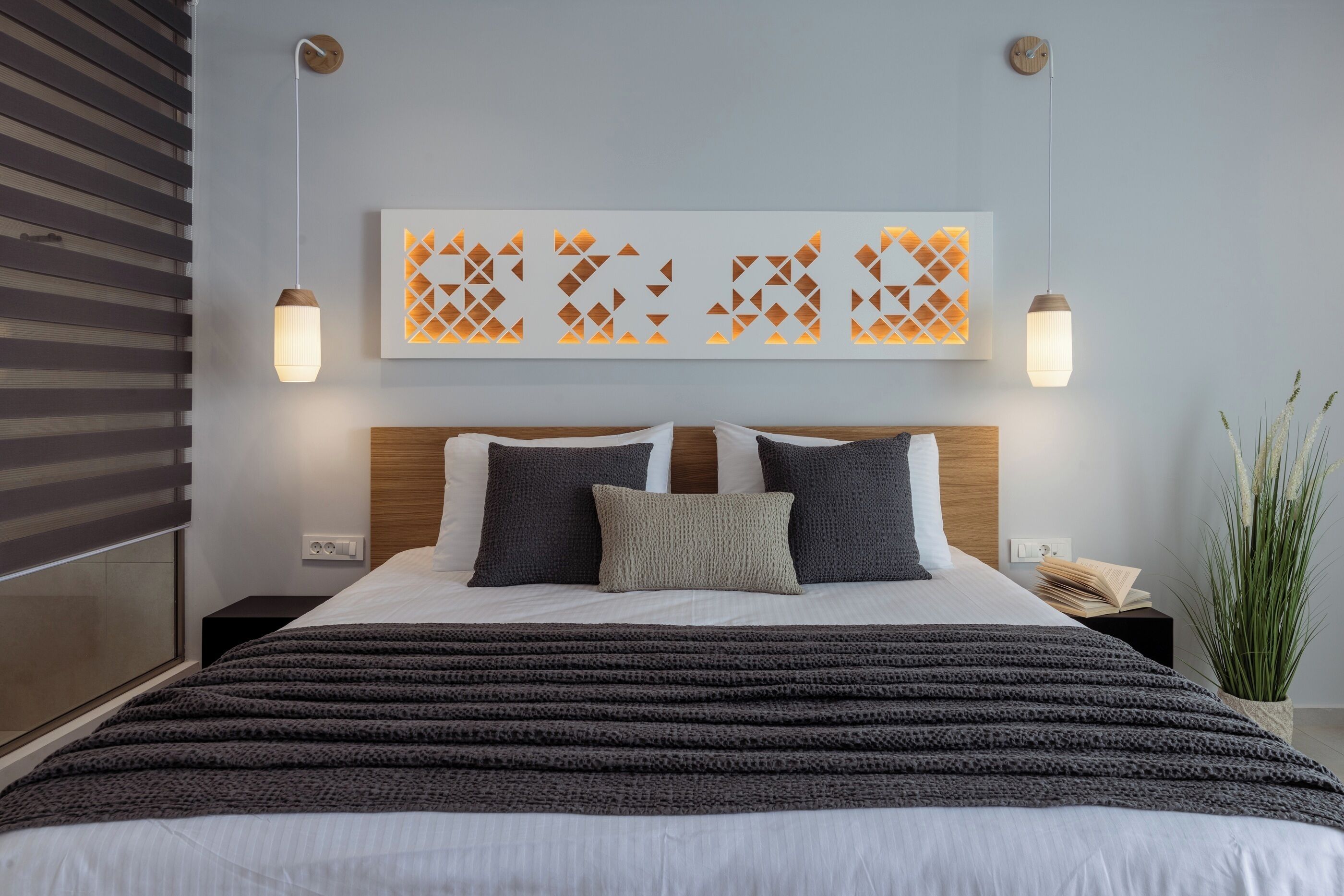 Un dormitorio moderno con una cama grande, dos mesitas de noche, una lámpara de pared y un panel decorativo.