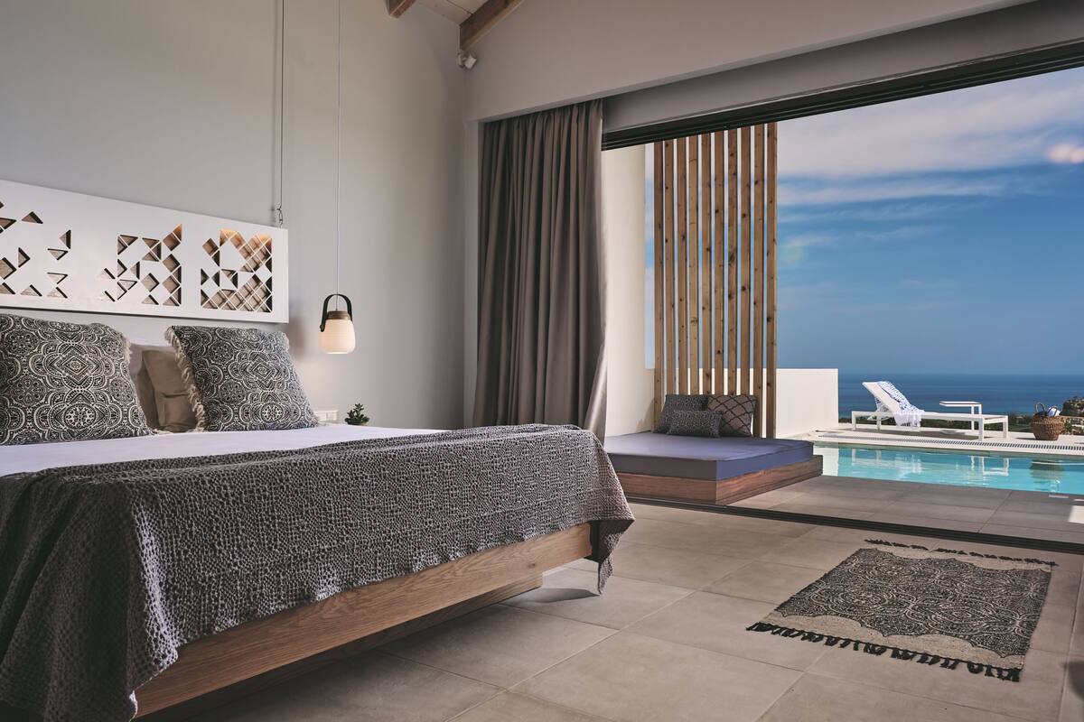 Un dormitori modern amb un llit gran, vistes a l'oceà i una zona de piscina.