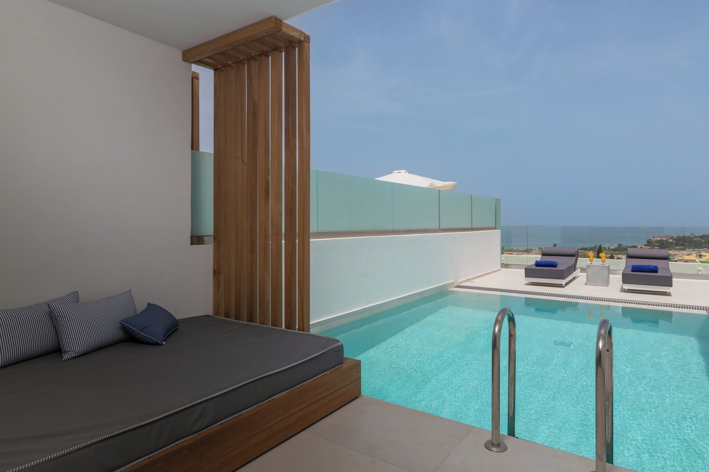 Een moderne hotelkamer met een zwembad, een bank met kussens en uitzicht op zee.