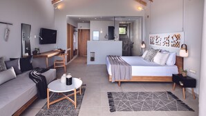 A modern bedroom with a large bed, a desk, and a sofa. There is a bathroom visible through an open door.