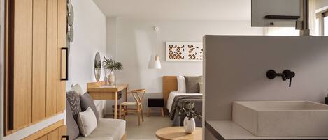 Un espace de vie moderne et compact, comprenant une armoire en bois, un coin repas, un lit avec une tête de lit, une petite table avec un vase et un évier intégré.