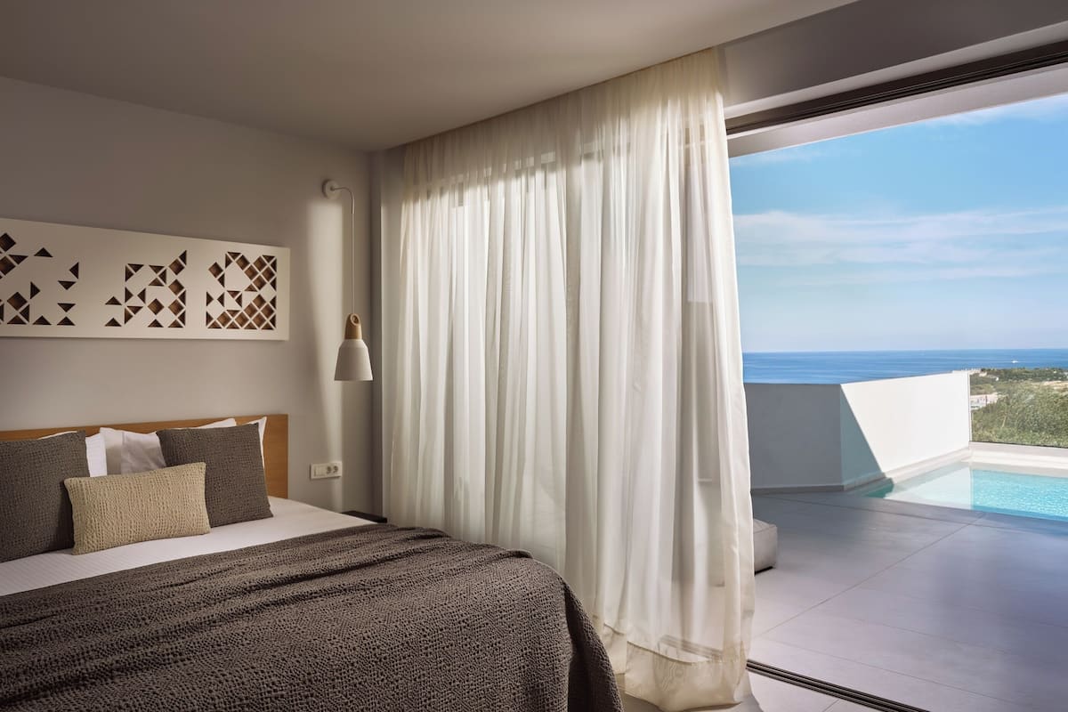 Una habitació d'hotel moderna amb un llit gran, vistes a l'oceà i un balcó amb piscina.