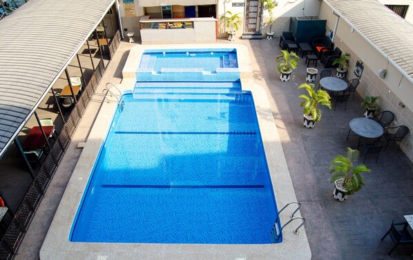 Zona de piscina en la azotea con varias piscinas, mobiliario exterior y plantas en macetas.