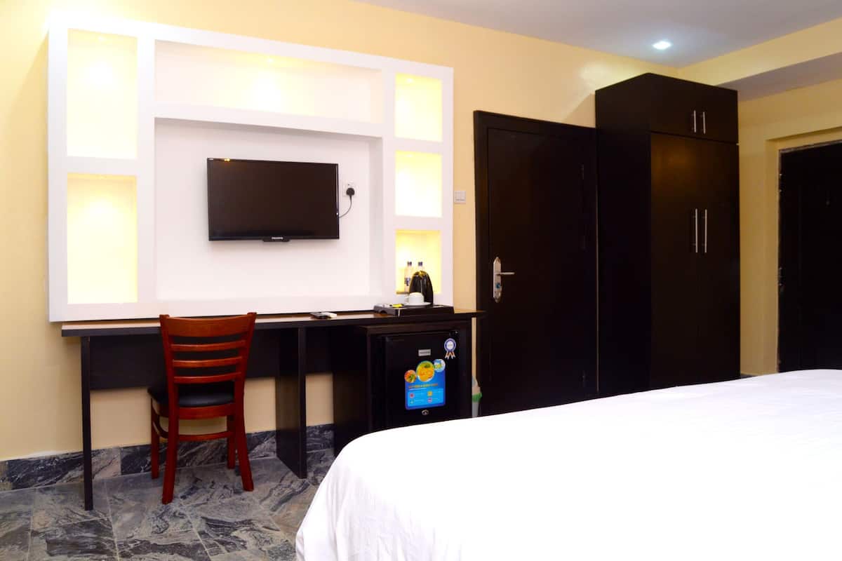 A hotel room with a bed, a desk with a chair, a TV mounted on the wall, and a wardrobe.