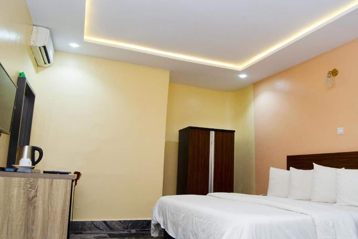 A hotel room with a bed, a wardrobe, a desk with a coffee maker, and an air conditioning unit.
