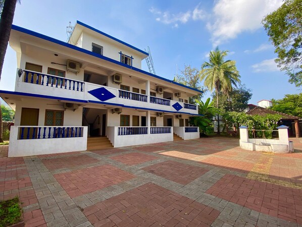 A two-story building with a blue and white exterior, a covered entrance, and a paved courtyard. - Anjuna Blue Resort (Anjuna)