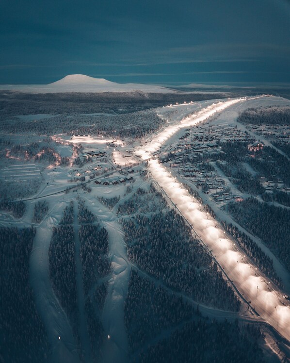 An aerial view of a snow-covered landscape with a road running through it, surrounded by dense forests and a distant mountain.