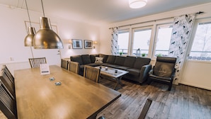 A modern living room with a wooden dining table, a sofa, and a coffee table. There are two pendant lights above the table and a window with curtains. - Idre Fjäll Stugor och Lägenheter (Idre)