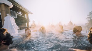 Un grupo de personas en un jacuzzi al aire libre, frente a un edificio de madera con un letrero que dice 'Fernilla Wiberg Hotel'.