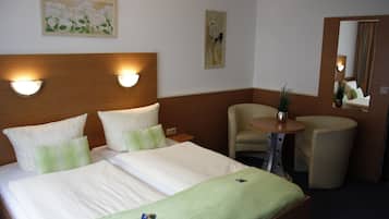 A hotel room with a double bed, two bedside lamps, a small round table, a chair, and a mirror.