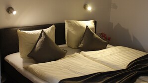 A neatly made bed with pillows and a blanket, a wall-mounted painting of a beach scene, and two wall-mounted lights. - Hotel Pellmühle (Jever)