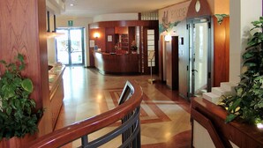 A hotel lobby with a reception desk, a staircase, and a reception area with a sign that reads "EXCEED". - Hotel Excelsior (Cervia)