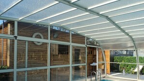A swimming pool with a glass enclosure, wooden walls, and a metal roof. - Hotel Excelsior (Cervia)