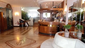 A hotel lobby with a curved reception desk, a white sofa, and a staircase leading to an upper floor. - Hotel Excelsior (Cervia)