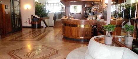 A hotel lobby with a curved reception desk, a white sofa, and a staircase leading to an upper floor.